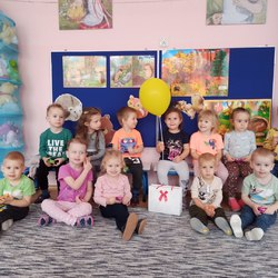 grupa przedszkolaków pośrodku siedzi dziewczynka z żółtym balonem.jpg